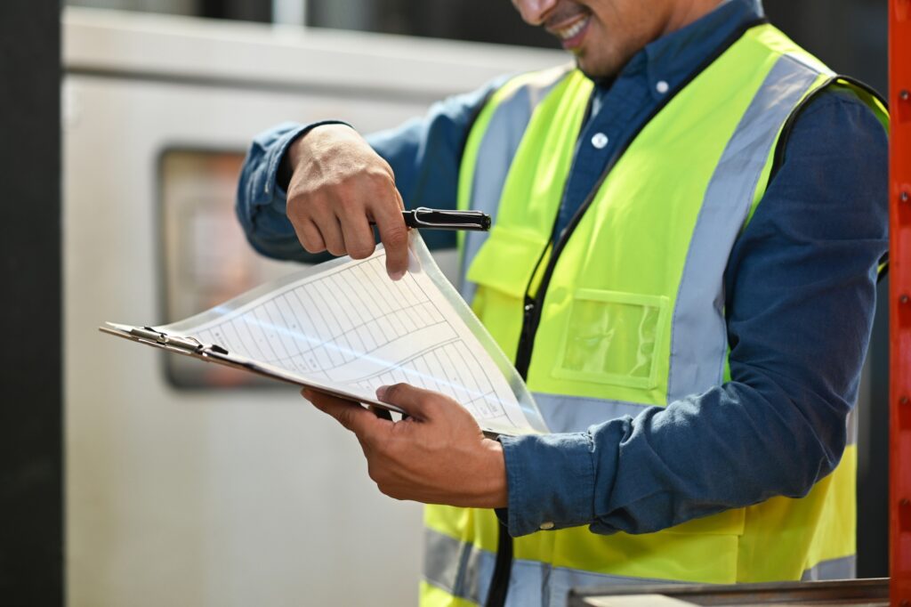 Male warehouse manager holding clipboard checking quantity of storage product in a large warehouse.